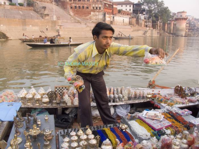 VARANASI UTTAR PRADESH INDIA November Hawker trying to sell  souvenirs to visitors travelling along the River Ganges viewing the historic Ghats - stepped embankments