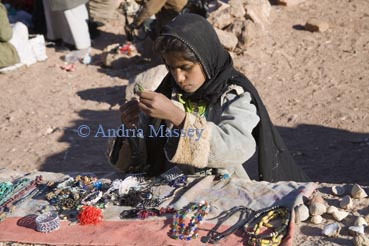 Sinai Desert Egypt North Africa February A young Bedouin girl sorting out trinkets laid out on a wall for sale to passing tourists